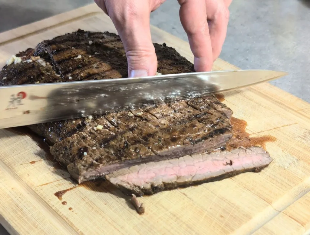 Flank steak that has been marinaded in Flank Steak Marinade being sliced on a cutting board. 