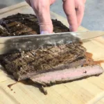 Flank steak being sliced on a cutting board.