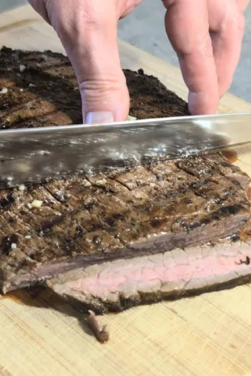 Flank steak being sliced on a cutting board.