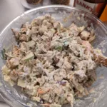 Chicken salad in a bowl with poppy seed buns and hot sauce in the background