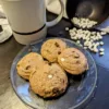 hot chocolate cookies on a plate with a cup of hot chocolate with marshmallows and a bowl of mini marshmallows spilled in the backround