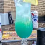 tropical lagoon cocktail with a lemon slice and a beer in the background