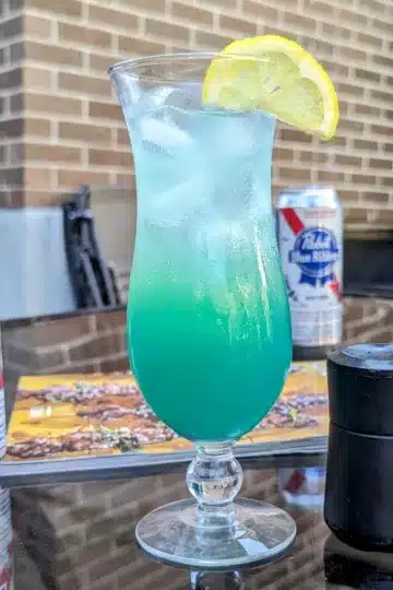 tropical lagoon cocktail with a lemon slice and a beer in the background