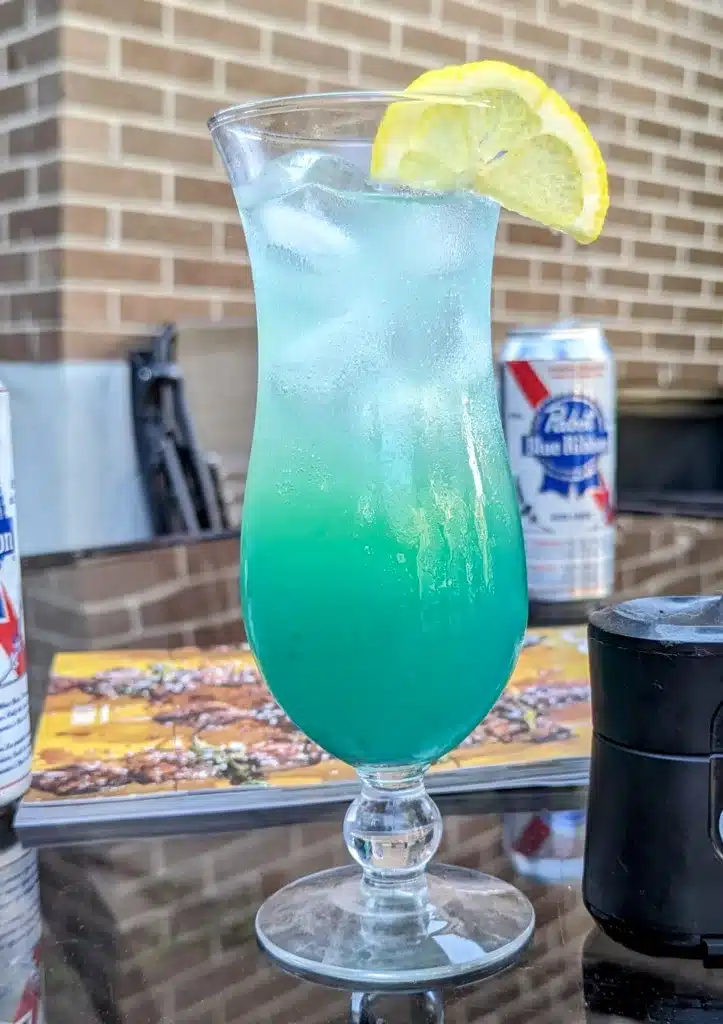 tropical lagoon cocktail with a lemon slice and a beer in the background