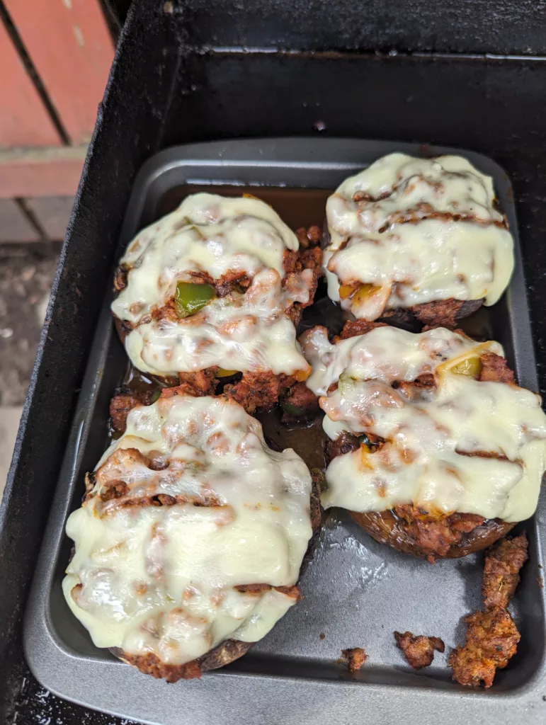 four stuffed portobello mushrooms on a tray on a blackstone griddle