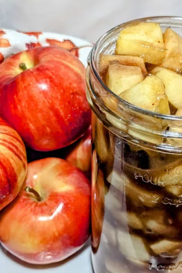 A jar of apple pie filling with a pile of apples to the left side.