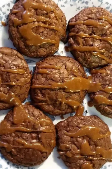 Seven brownie cookies with caramel drizzle on a plate.