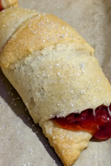 A cherry turnover on a parchment lined pan with sugar sprinkled on top.