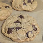 Three chocolate chunk cookies on parchment paper.