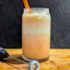 A glass of Orange creamsicle float with a milk frother in front of it.