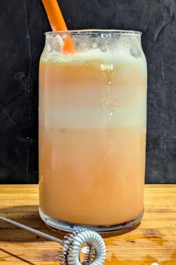 A glass of Orange creamsicle float with a milk frother in front of it.