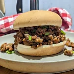 A Hawaiian loose meat sandwich on a plate with a red and white checkered napkin in the back.