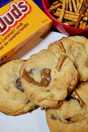 Milk dud pretzel cookies with a box of milk duds and a bowl of pretzels.