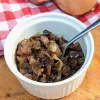 A ramekin filled with caramelized onion marmalade with a small spoon in it and a red and white checkered cloth in the background.