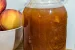 A jar of peach brandy sauce with a bowl of peaches to the left.
