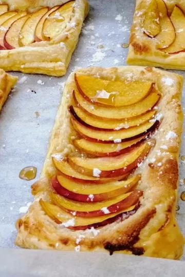 Peach Puff pastries on parchment paper with drizzles of maple syrup.