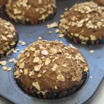 A close up view of a pumpkin muffin in a muffin tin with three muffins in the background.