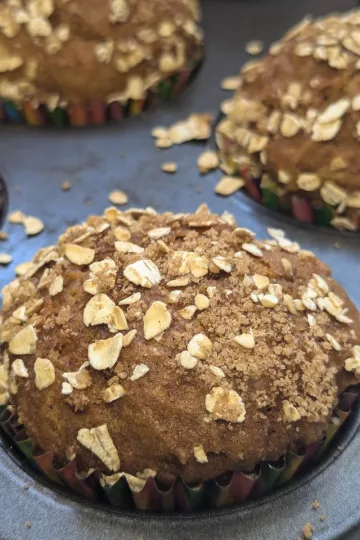 A close up view of a pumpkin muffin in a muffin tin with three muffins in the background.