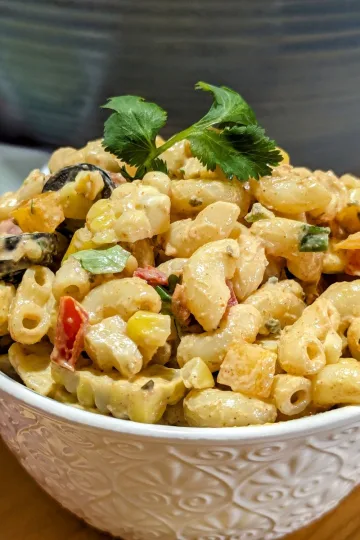 A bowl of tex mex macaroni salad with a sprig of cilantro on top and a half of a lime in the background on the left.