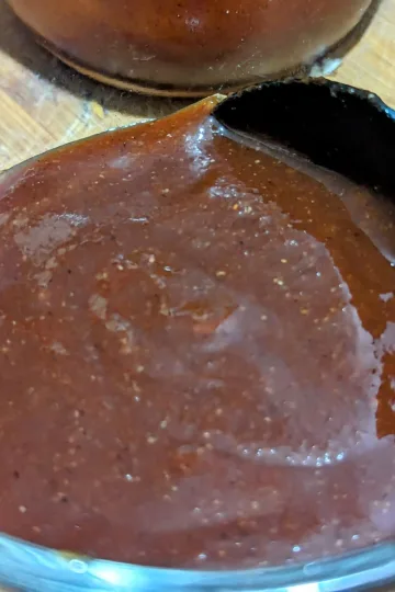 A bowl of apple cider BBQ sauce with a black spoon in it.