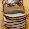Apple Cider brined pork loin sliced on a wooden cutting board.