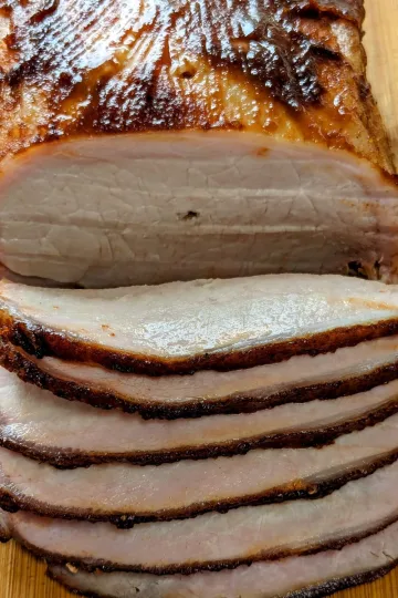 Apple Cider brined pork loin sliced on a wooden cutting board.