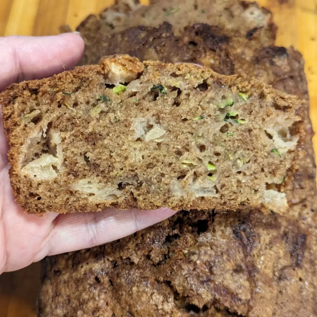 A slice of apple zucchini bread held over a loaf.