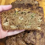 A slice of apple zucchini bread held over a loaf.