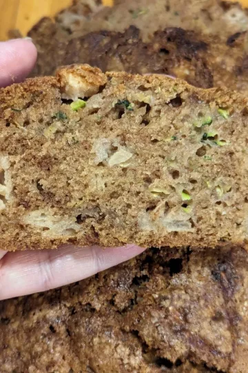 A slice of apple zucchini bread held over a loaf.