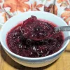 A bowl of boozy cranberry sauce with a spoonful of sauce over the bowl.