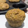 A carrot muffin in front of a pan of muffins.