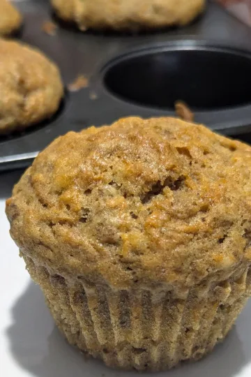 A carrot muffin in front of a pan of muffins.