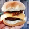 Chili cheeseburger held in a hand on front of a fence.