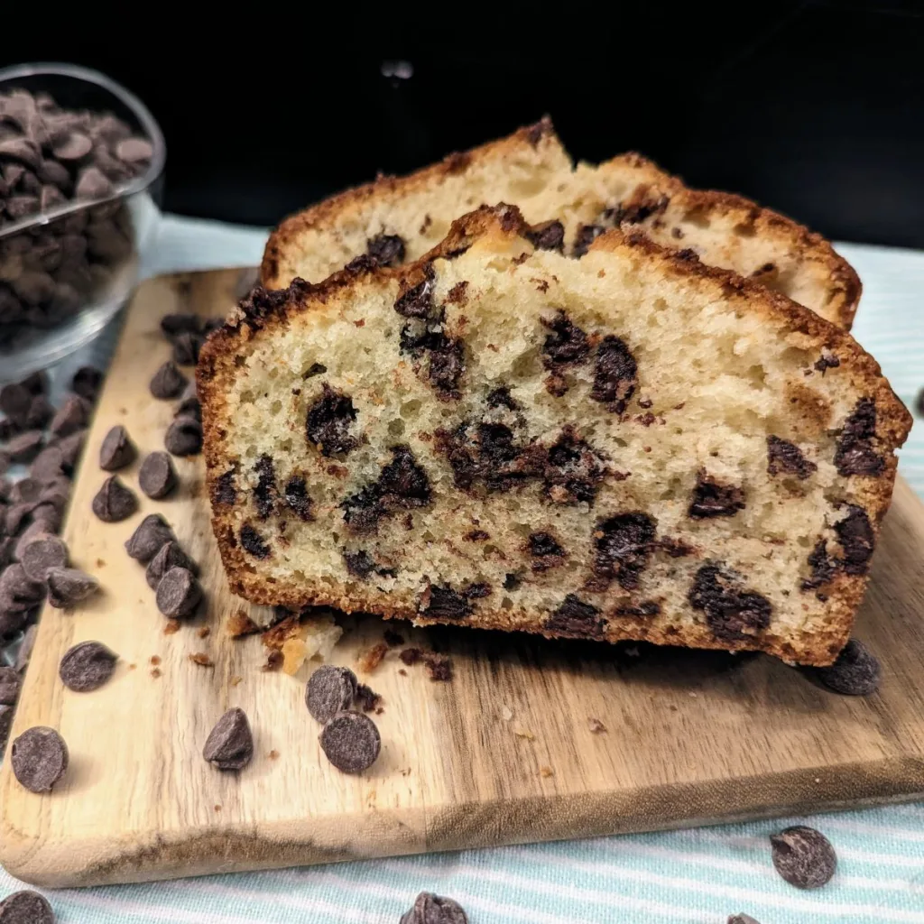 Chocolate chip bread slices on a small square cutting board with a bowl of chocolate chips behind to the left.