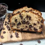Chocolate chip bread slices on a small square cutting board with a bowl of chocolate chips behind to the left.