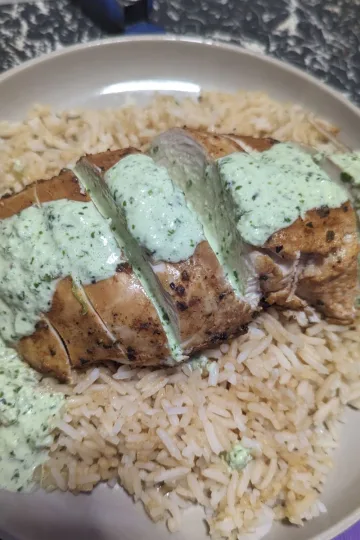A plate of rice with a chicken breast on top that is covered in Cilantro lime sauce.