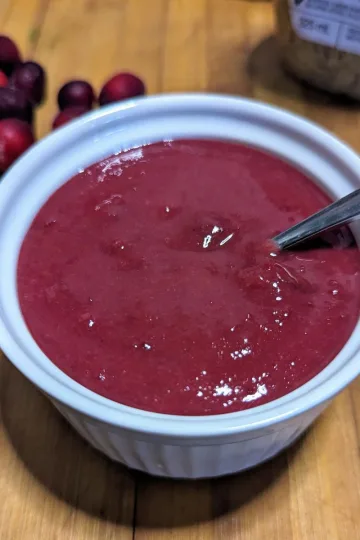 A small bowl of cranberry mustard sauce with a small spoon in it. There are fresh cranberries off to to left.