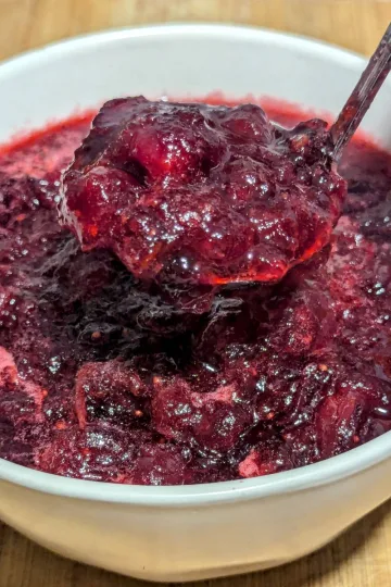 A white bowl filled with homemade cranberry sauce with a spoonful of cranberry sauce held over the bowl.