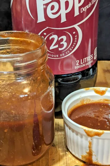A white ramekin of Dr Pepper rib sauce with a jar half filled with sauce on the left and a bottle of Dr Pepper behind it.