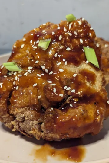 Fried chicken coated in gochujang sauce with sesame seeds and green onions sprinkled over.