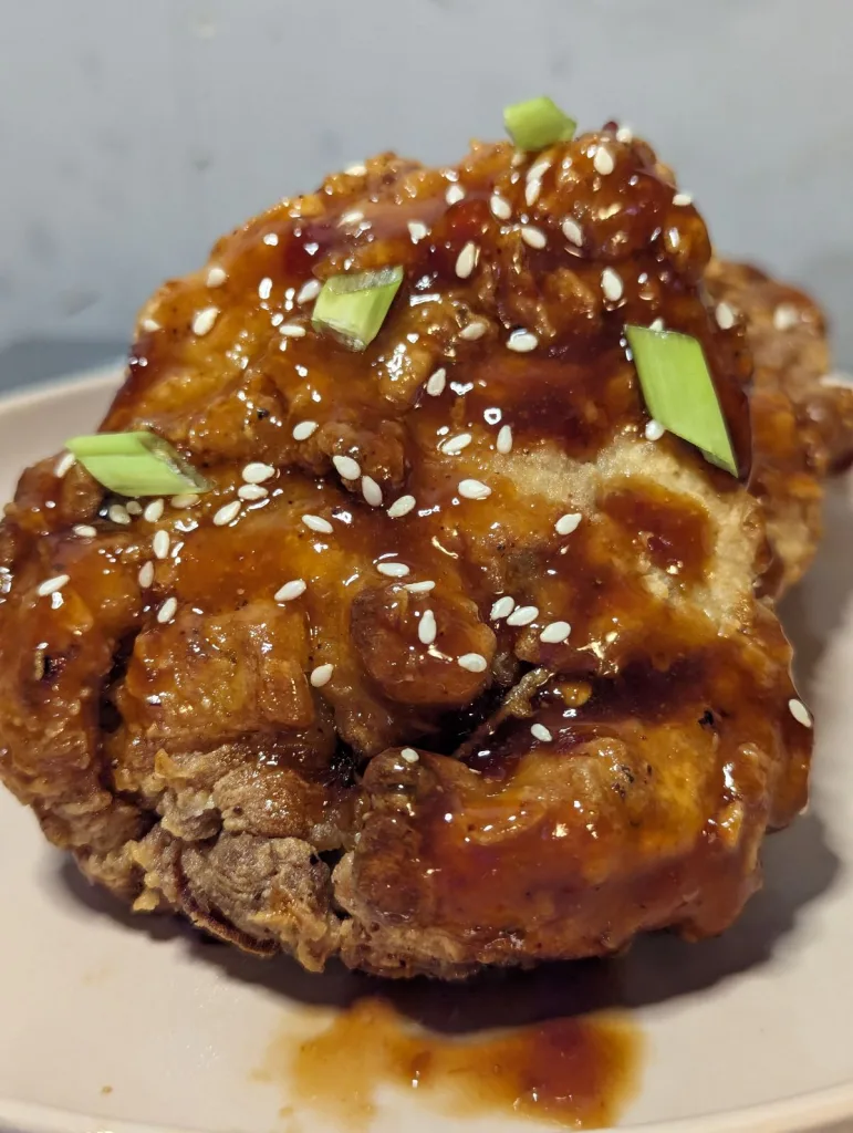 Fried chicken coated in Sweet and Spicy Gochujang Sauce with sesame seeds and green onions sprinkled over.