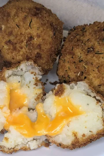 A plate of three potato bombs. The front one is cut in half and the melted cheese is oozing out.
