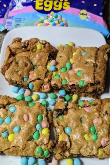 Four Mini egg cookie bars with a bag of mini eggs in the back.