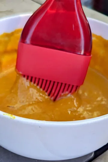 A bowl of sriracha mustard sauce with a red basting brush dipped in it.
