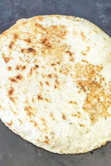 A tortilla cooking on a flat top.