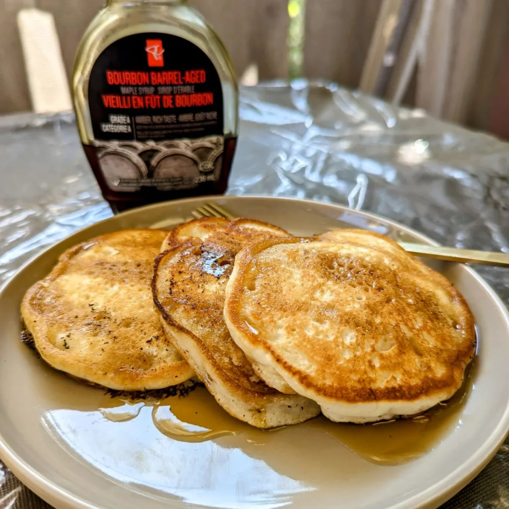 A plate with three pancakes fanned out and a bottle of maple syrup behind the plate.