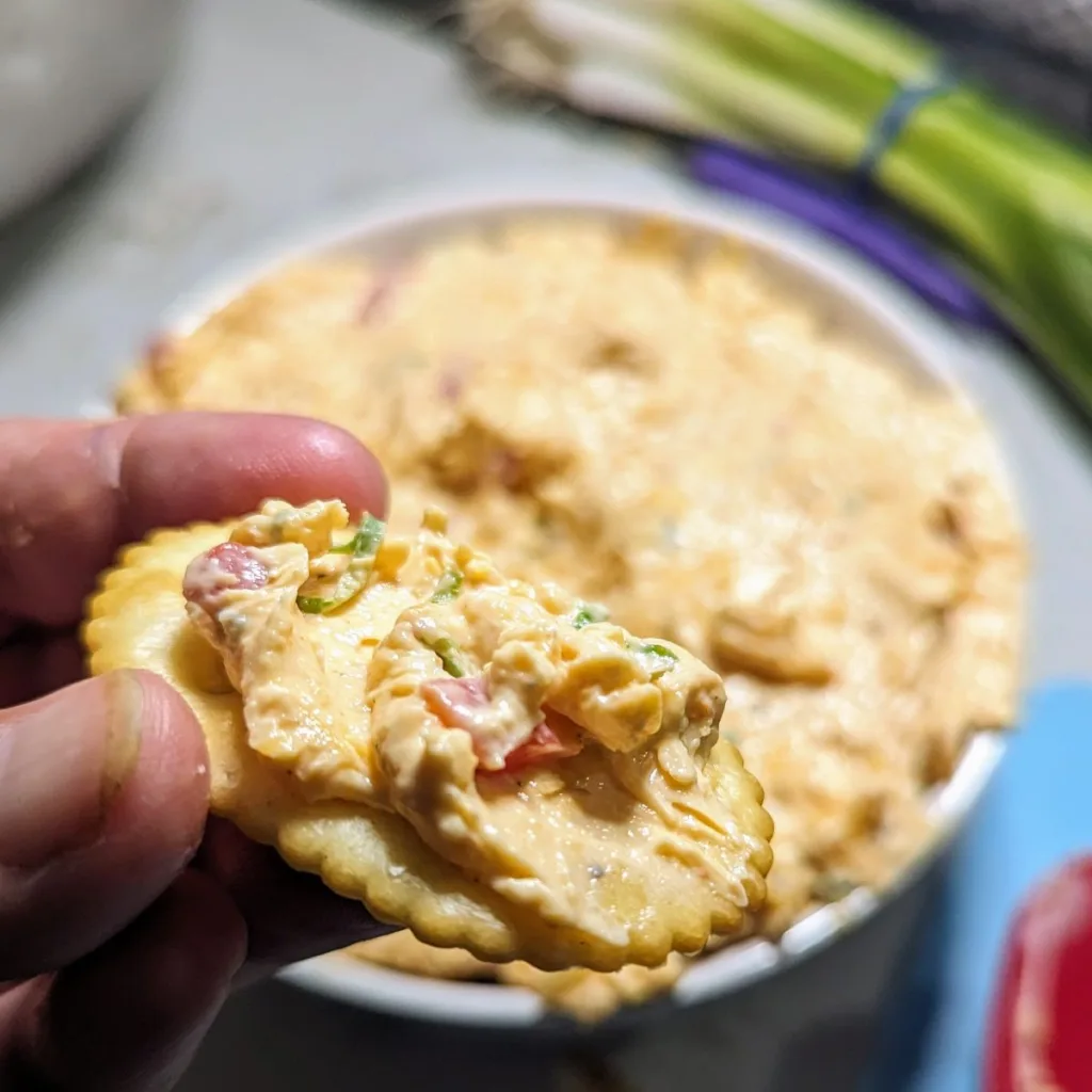 A cracker with Easy Homemade Pimento Cheese being held over the bowl of pimento cheese.