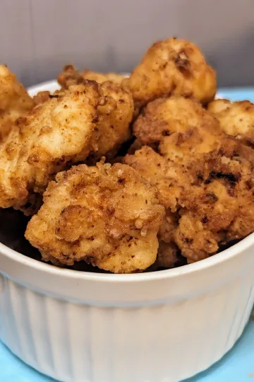 A small white bowl filled with homemade popcorn chicken.