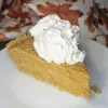A slice of pumpkin chiffon pie topped with whipped cream. There is a cloth with fall leaves in the background.