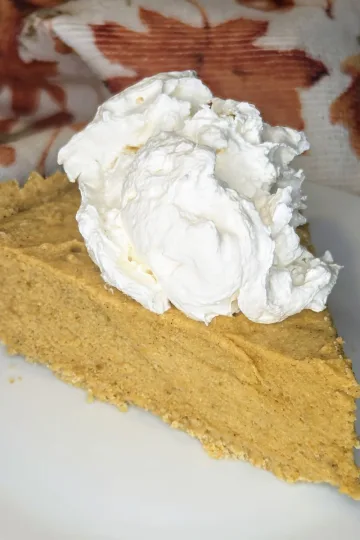A slice of pumpkin chiffon pie topped with whipped cream. There is a cloth with fall leaves in the background.